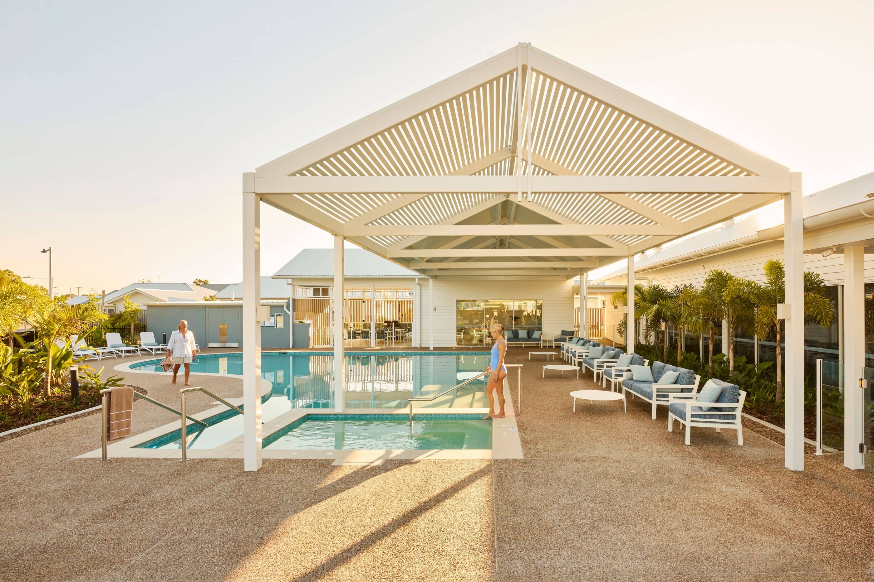 Ingenia Lifestyle community pool with two residents, shaded outdoor seating, and a modern clubhouse facility.