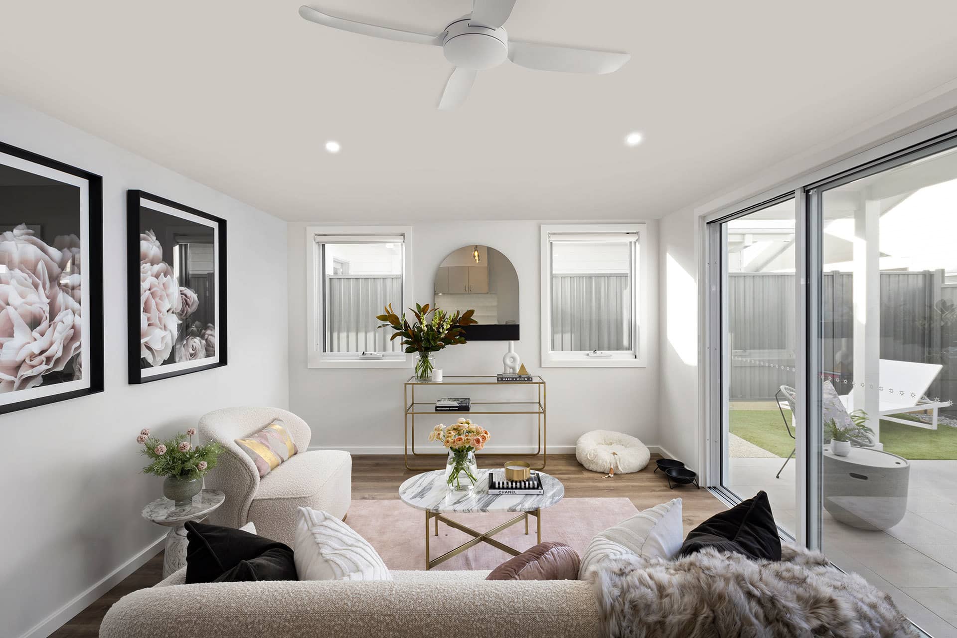 A modern living room with plush seating, marble coffee table, and large windows opening to a backyard.
