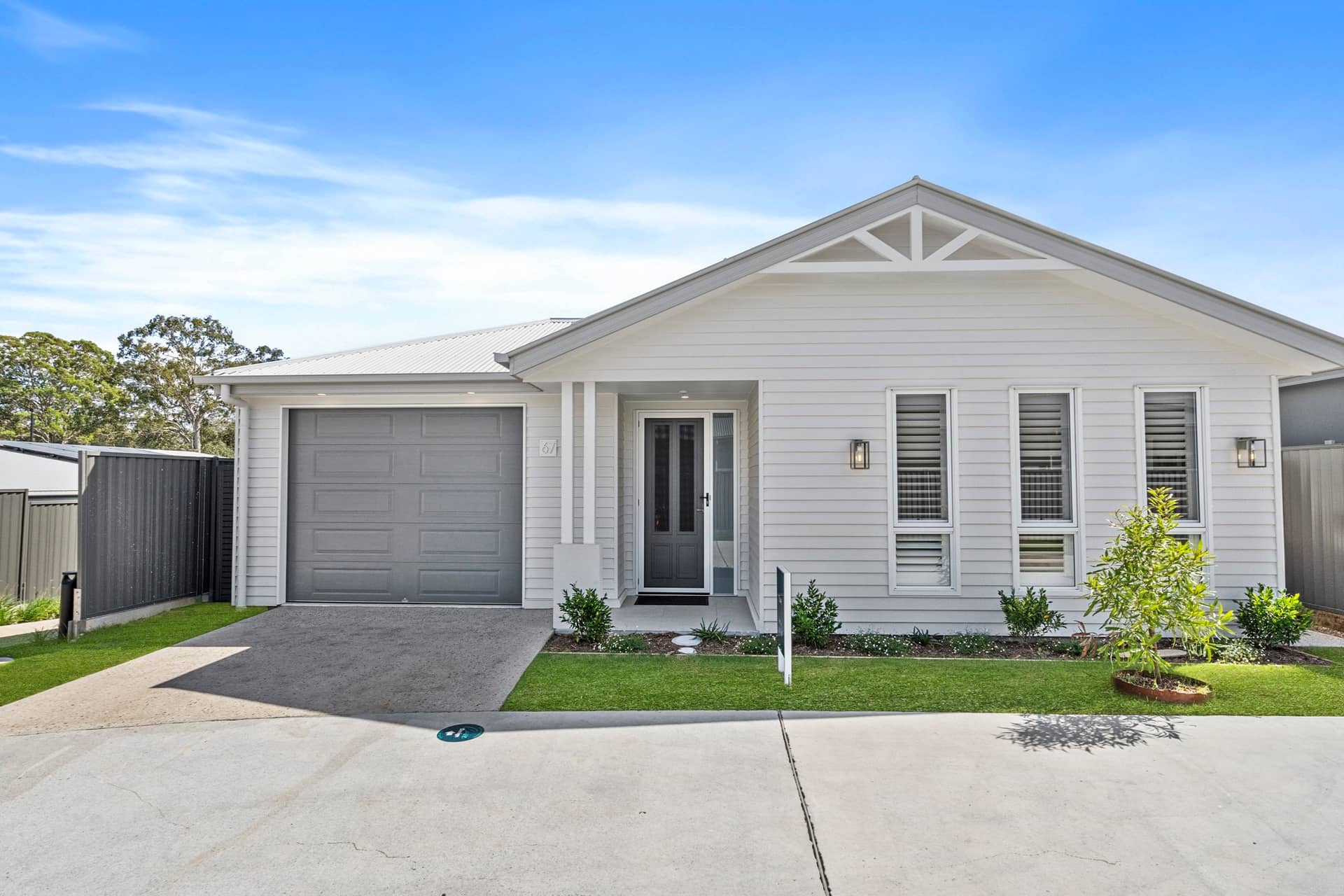 Exterior view of a light grey, single-story land lease home with a grey garage door and white cladding.