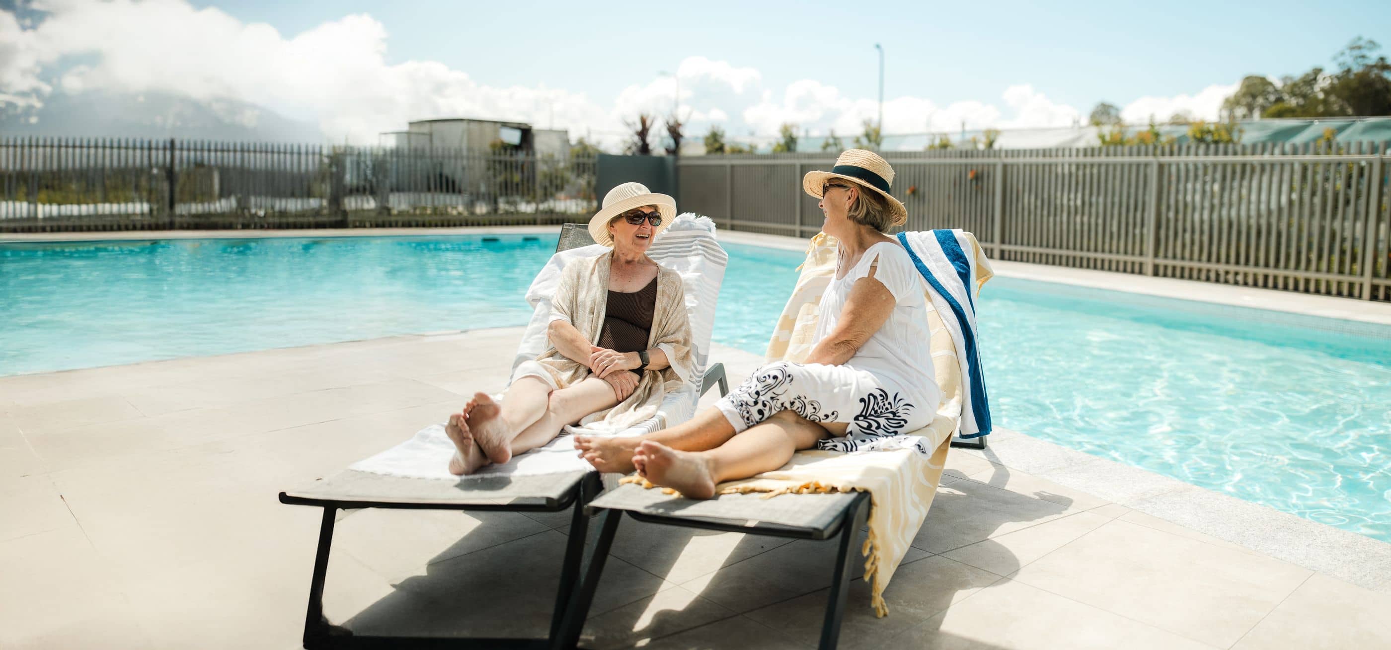 Two women relax on lounge chairs beside a sparkling blue swimming pool at an Ingenia Lifestyle community.