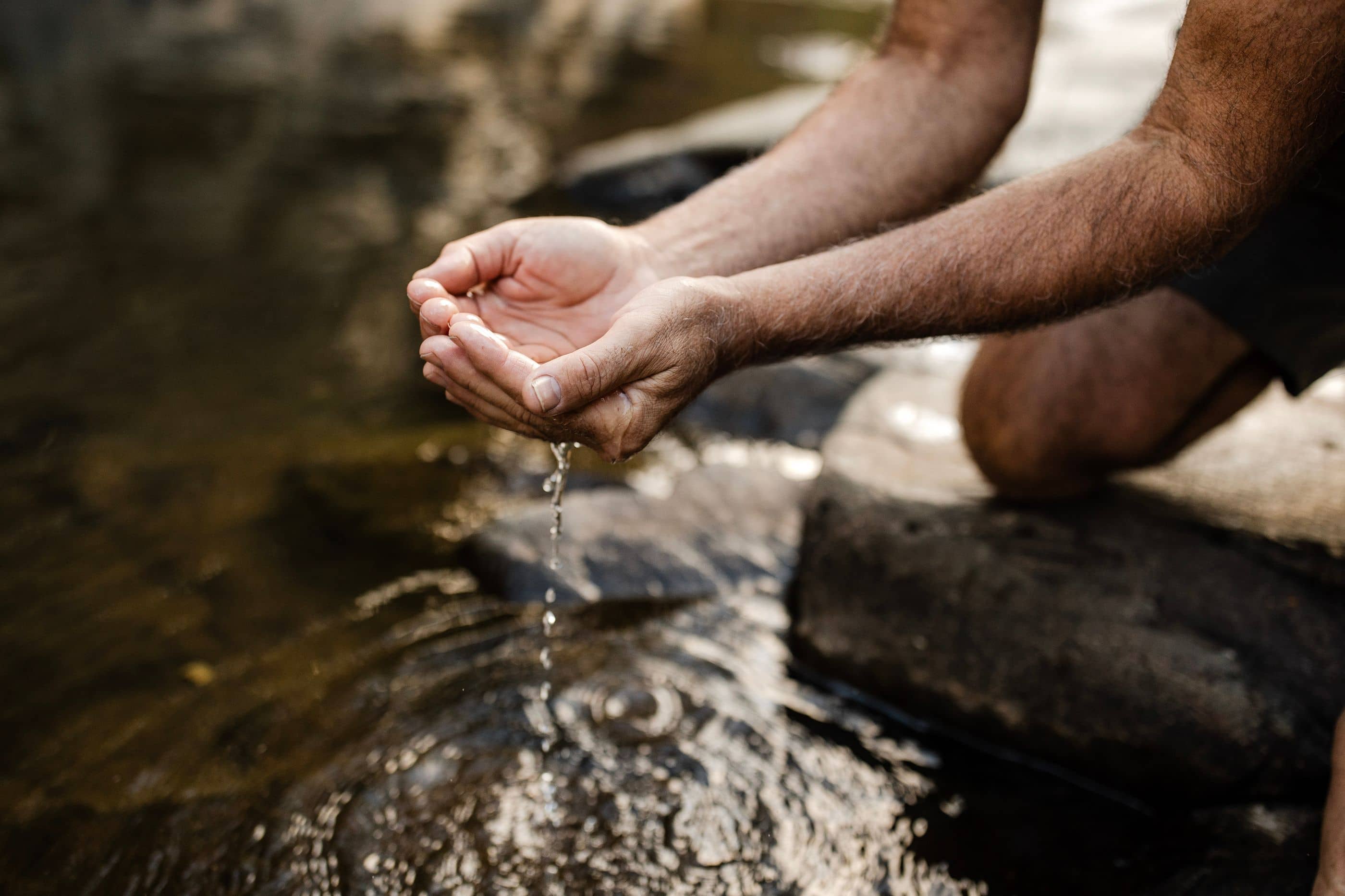 Cupped hands collecting dripping water next to rocks.