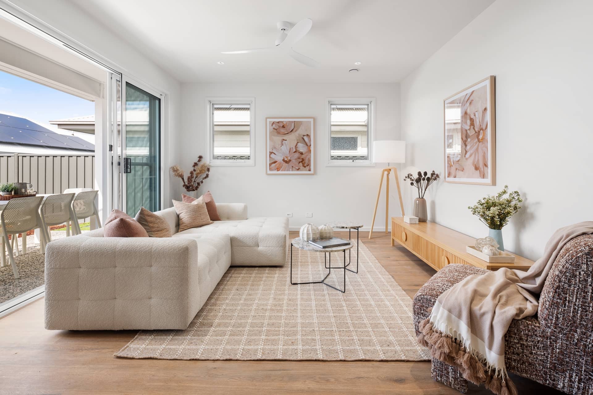 A modern Ingenia Lifestyle home living room with a white sofa, entertainment unit, and a patio with outdoor seating. Solar panels visible on roof.