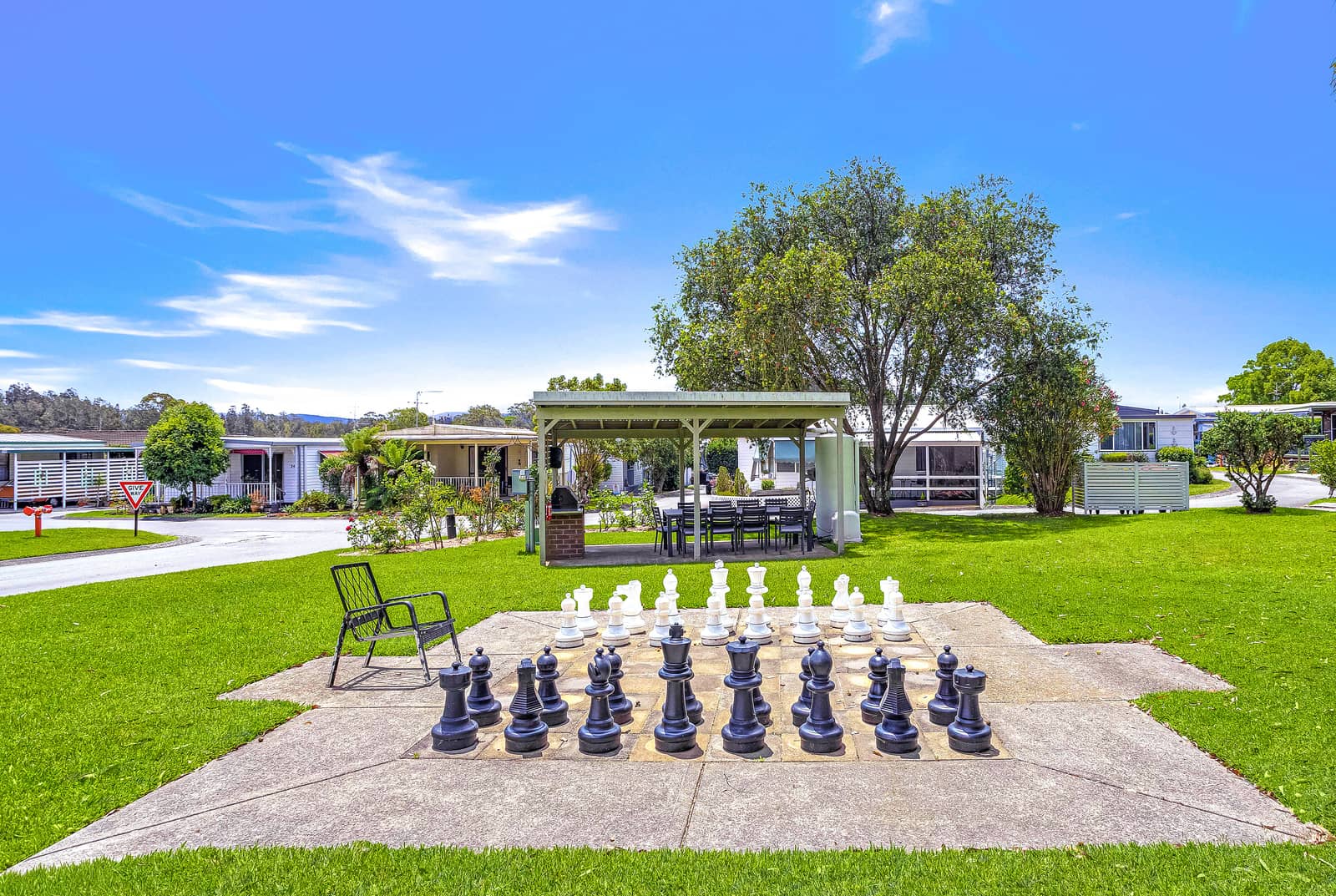 Large outdoor chess set with black and white pieces on a concrete base in a grassy area of an Ingenia Lifestyle community.