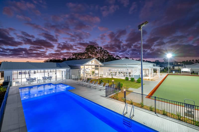 An Ingenia Lifestyle community featuring a bright blue swimming pool and bowling green at dusk.