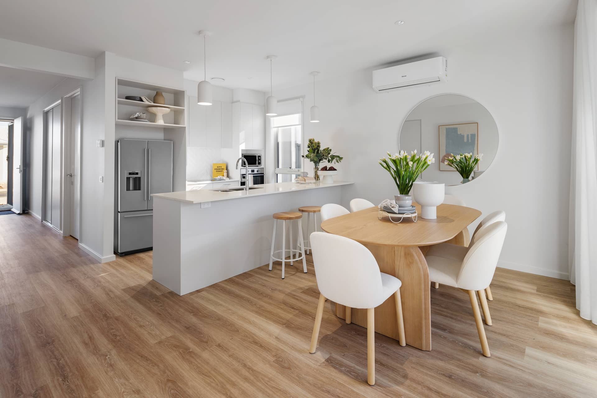 Open-plan kitchen and dining area in an Ingenia Lifestyle home, with white cabinets, wooden floors, and a modern dining set.