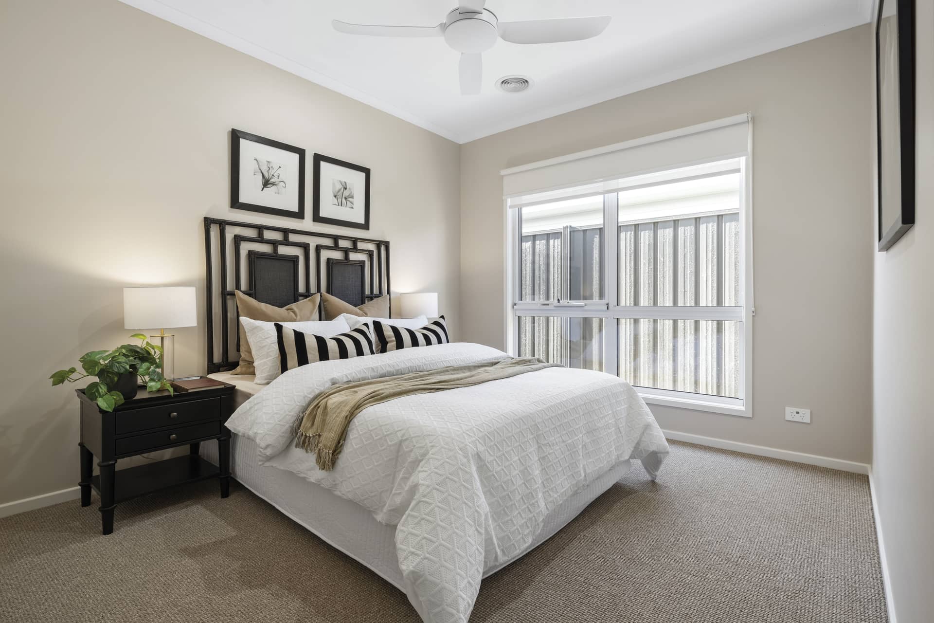 A neatly made bed with a textured white comforter in a light-colored bedroom, featuring a black metal headboard and bedside tables.
