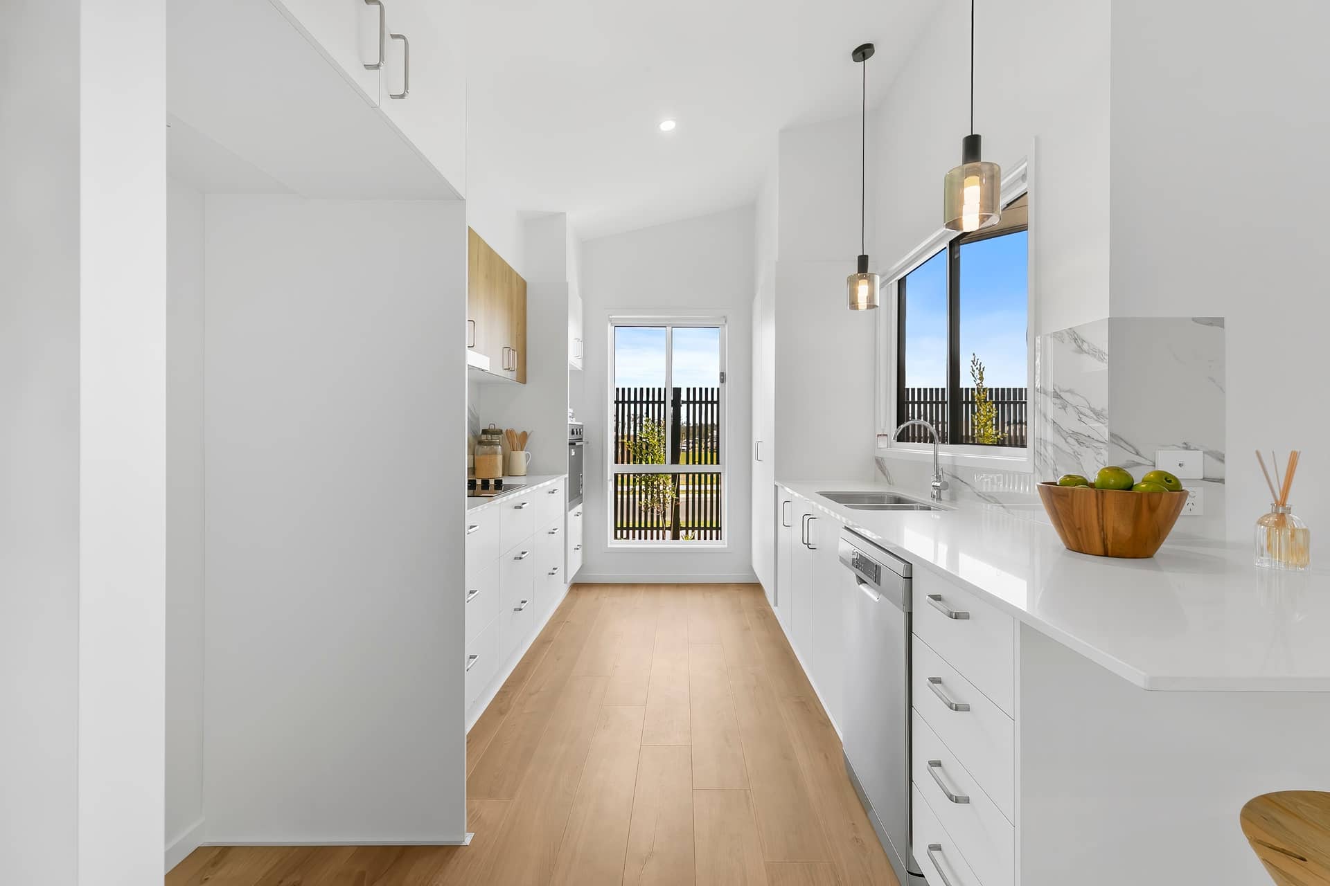 A modern kitchen in an Ingenia Lifestyle home, featuring white cabinetry, wooden floors, a sink, and two pendant lights.