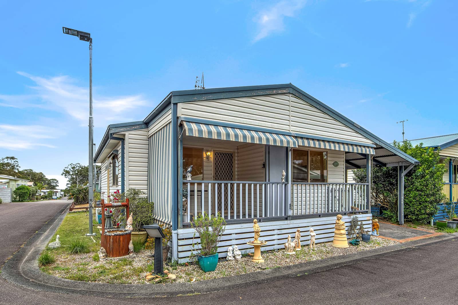 A land lease home with light siding, a striped awning over its porch, and a decorated low-maintenance garden in an Ingenia Lifestyle community.
