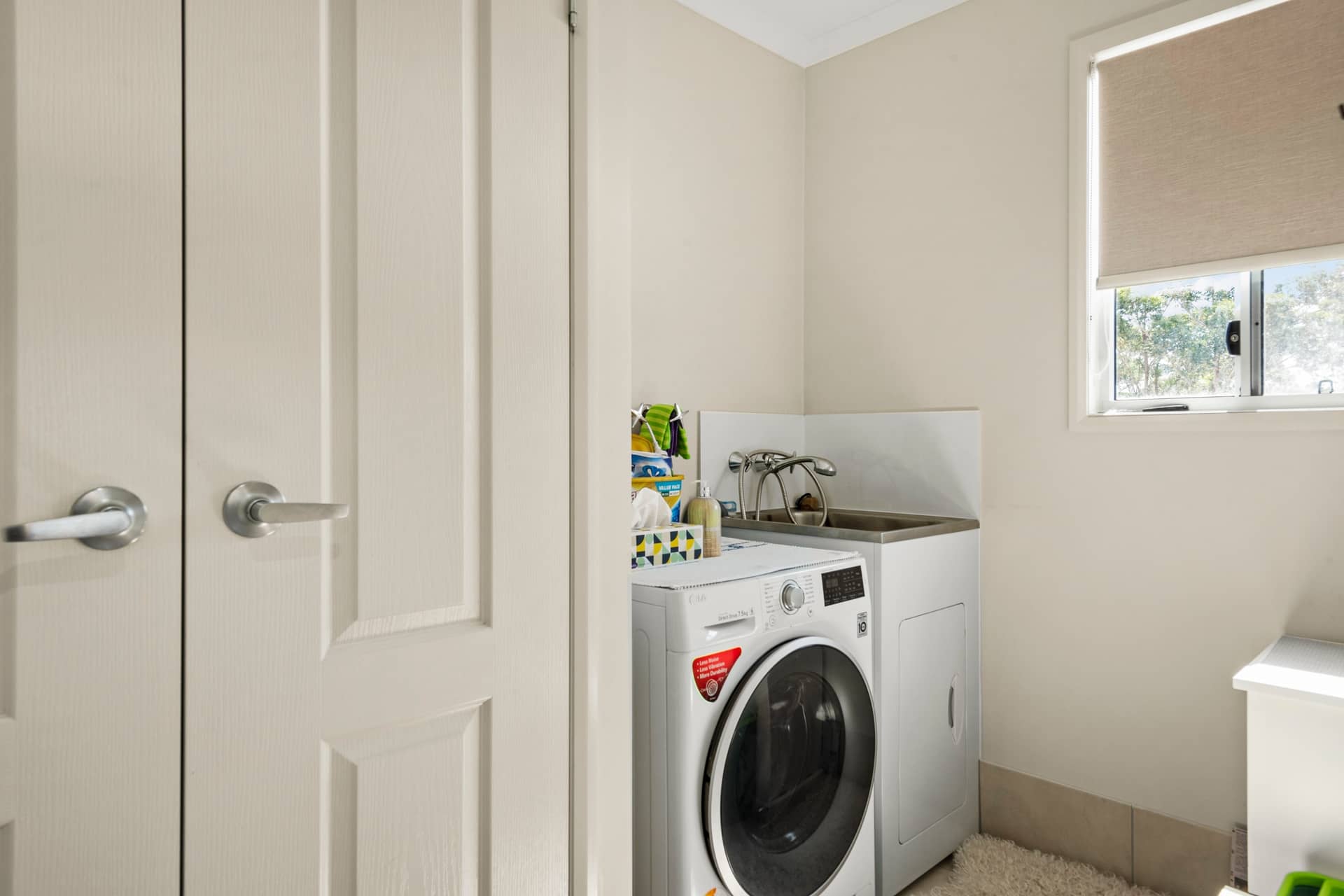 A laundry room in an Ingenia Lifestyle home with a washing machine, dryer, utility sink, and window.