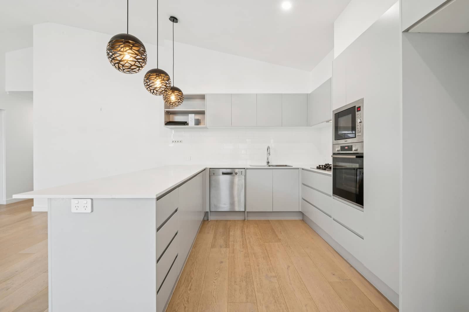Modern grey kitchen with white benchtop, stainless steel appliances, and decorative pendant lights.