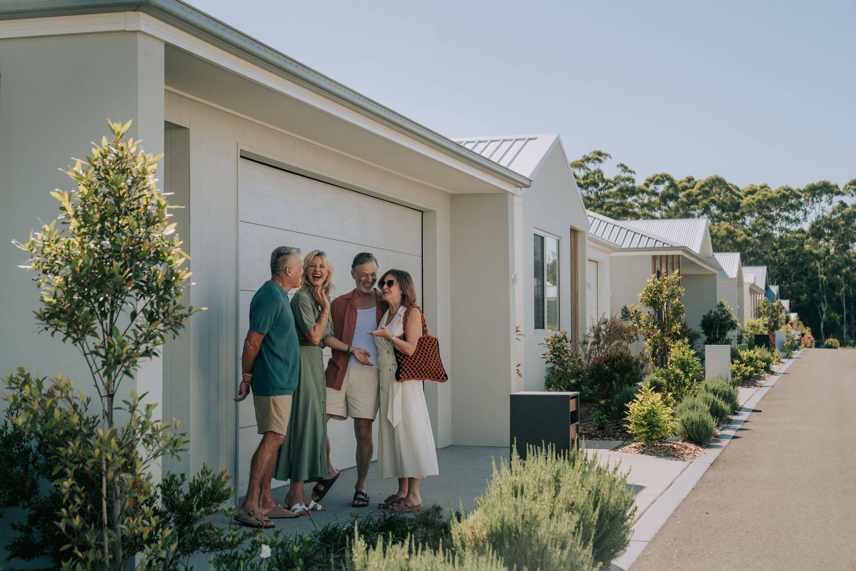 Four people talking and laughing in front of a modern Ingenia Lifestyle home with landscaped gardens.