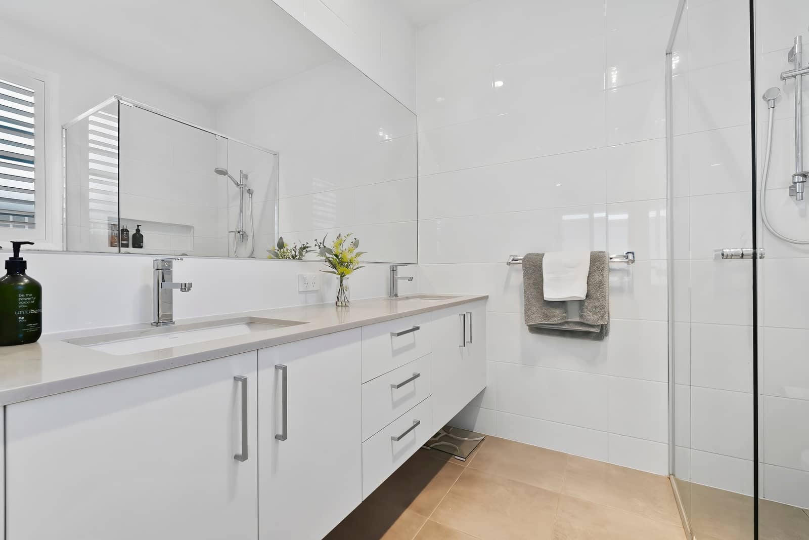 A contemporary Ingenia Lifestyle bathroom featuring a white dual vanity, chrome fixtures, white tiled walls, and a glass shower.