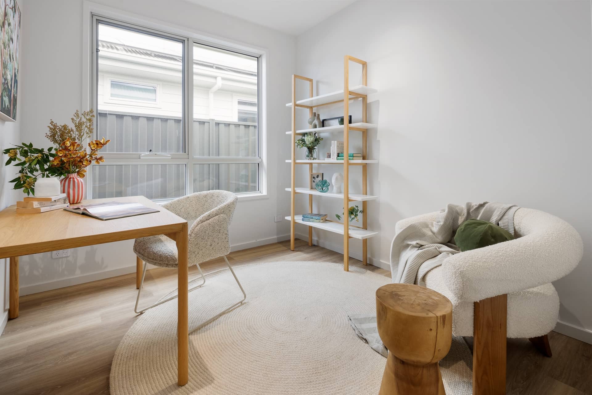 Bright home office in an Ingenia Lifestyle home, with a wooden desk, bouclé chair, contemporary bookshelf, and round rug.