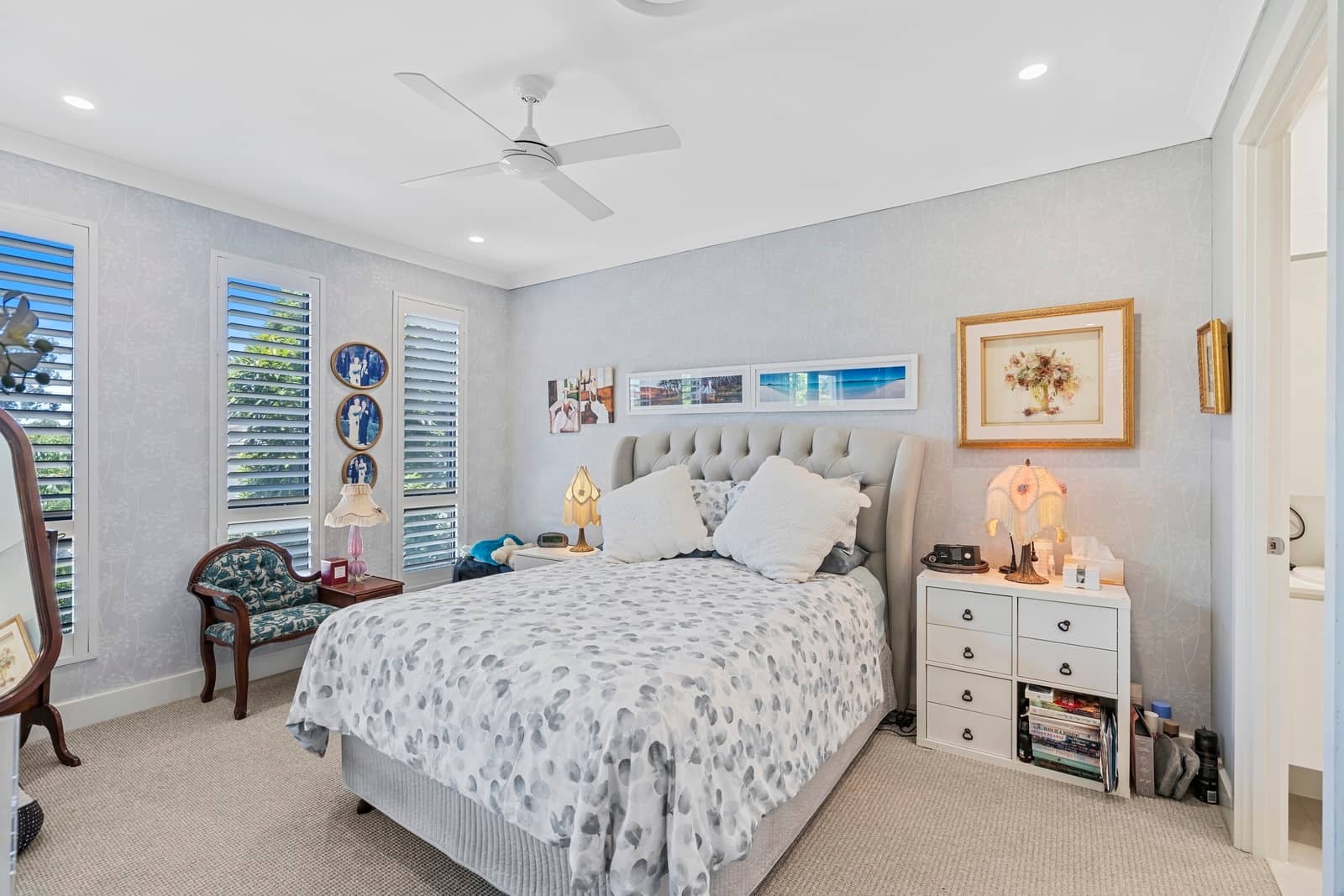 A light-filled bedroom with a queen bed, patterned bedding, and a tufted headboard in an Ingenia Lifestyle community.