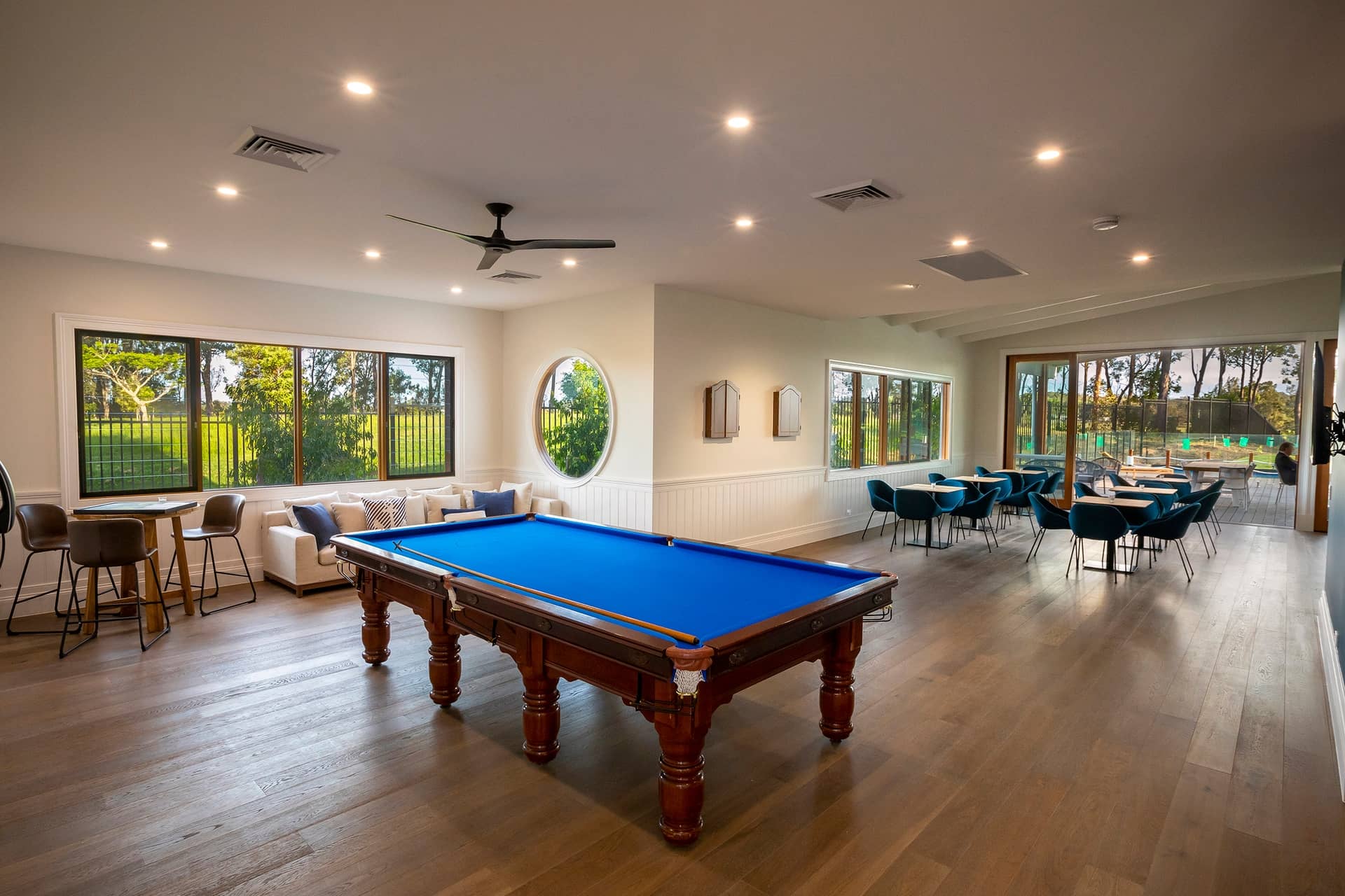 A spacious recreation room in an Ingenia Lifestyle community with a pool table, various seating areas, and large windows.