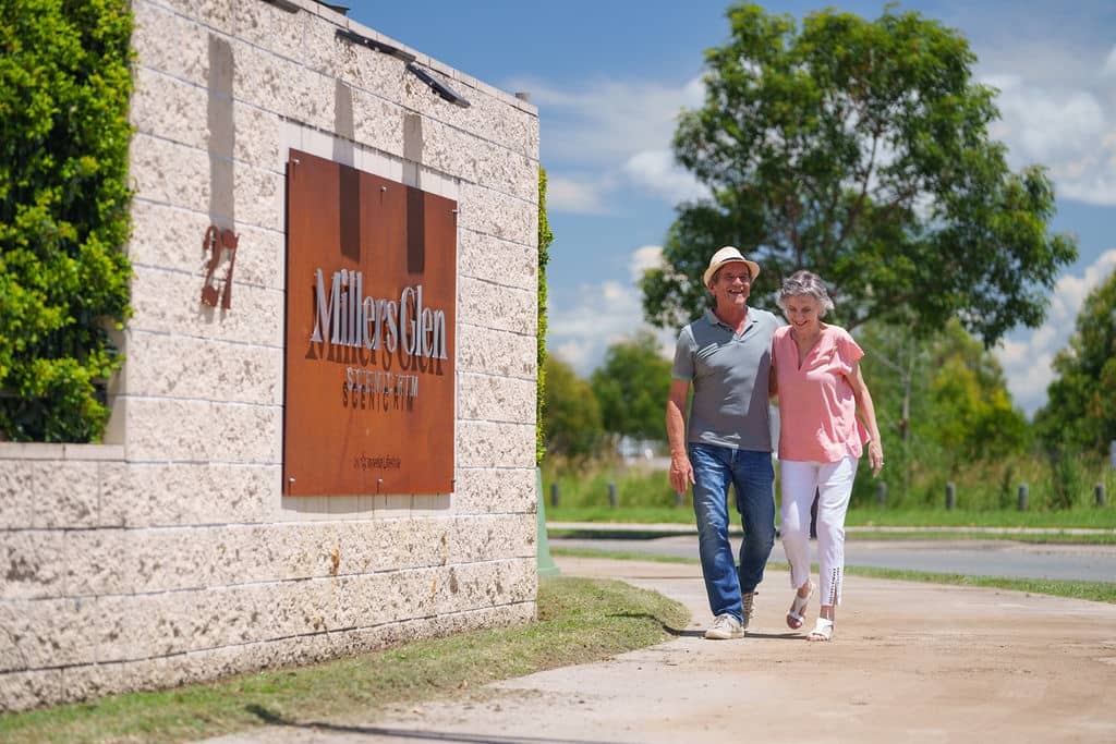 Two residents walk on a path past the Millers Glen Ingenia Lifestyle community sign on a sunny day.