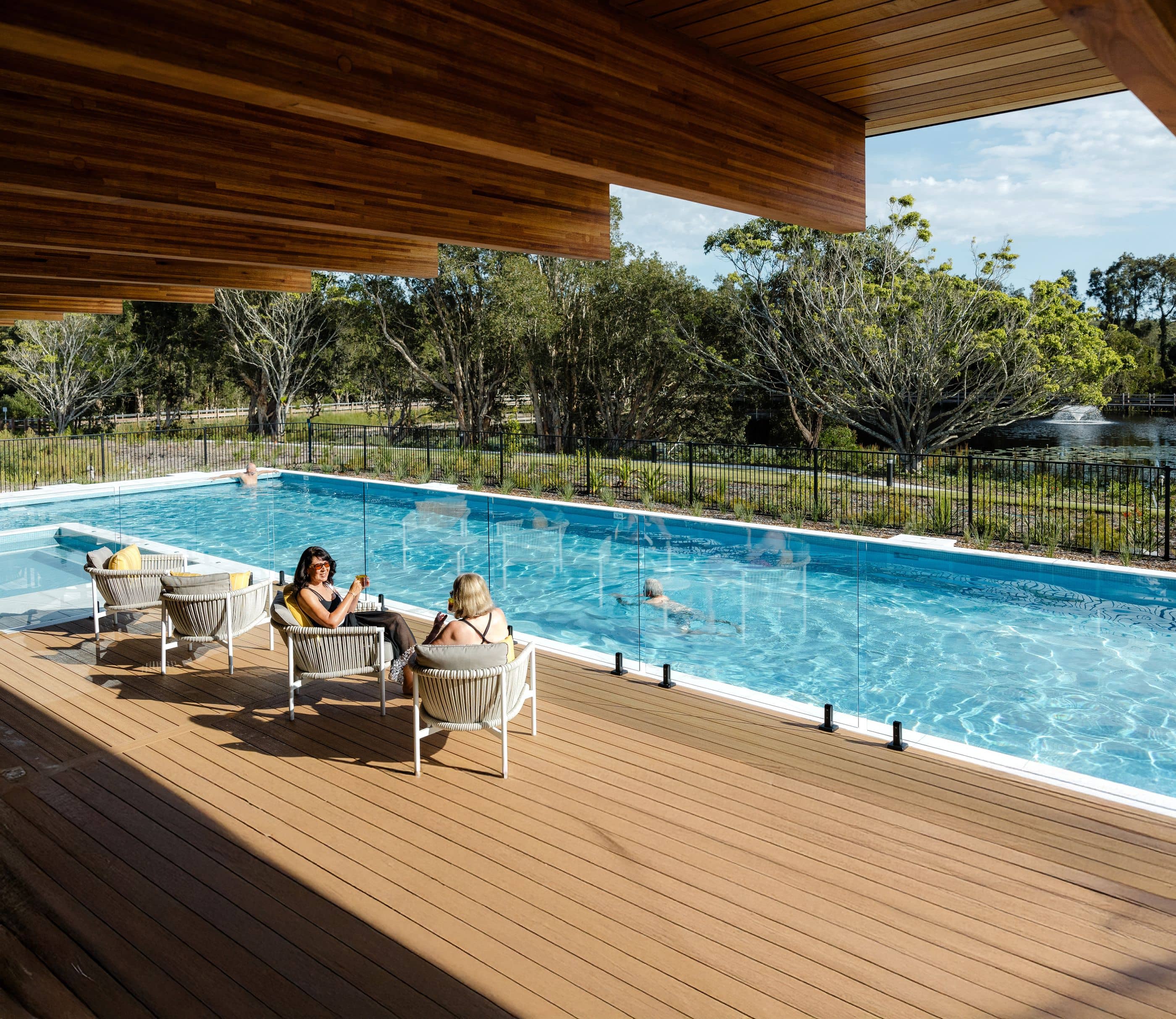 Ingenia Lifestyle community pool area with residents relaxing on the deck and swimming, surrounded by landscaped grounds.
