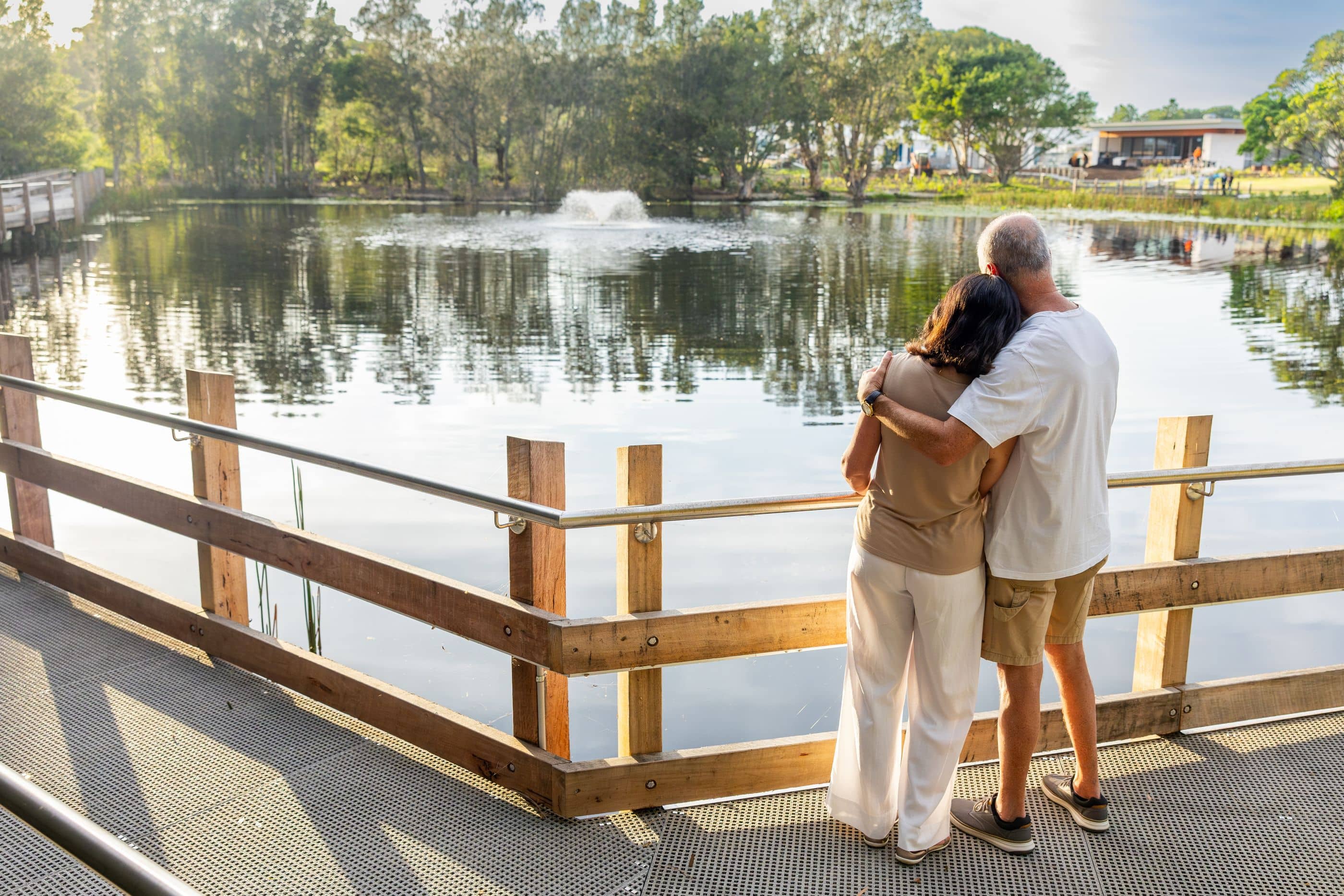 Couple embracing on a boardwalk overlooking a lake with a fountain in the Ingenia Lifestyle community.