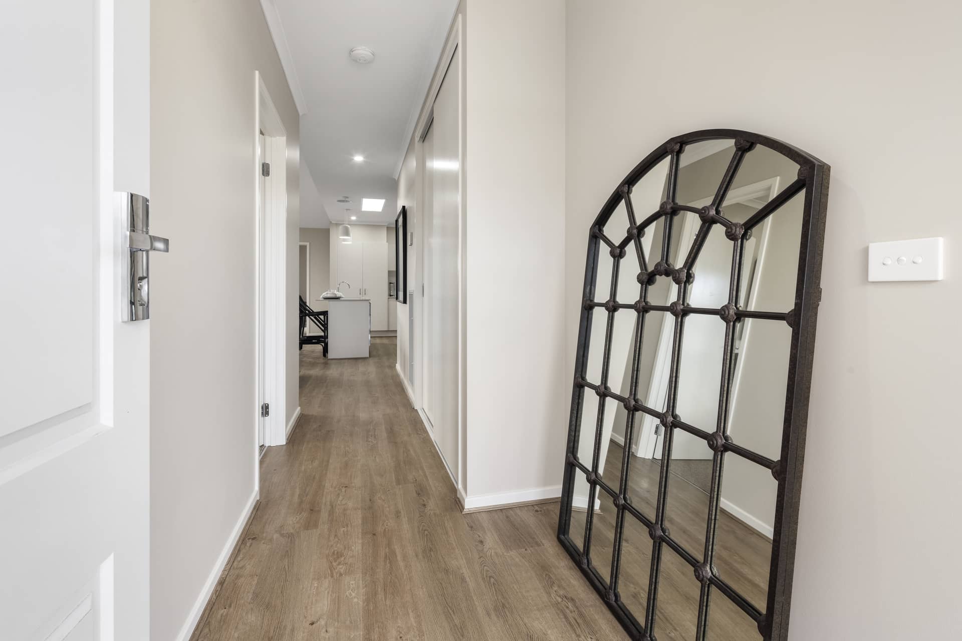 Hallway with wooden floors and an ornate mirror next to a doorway.