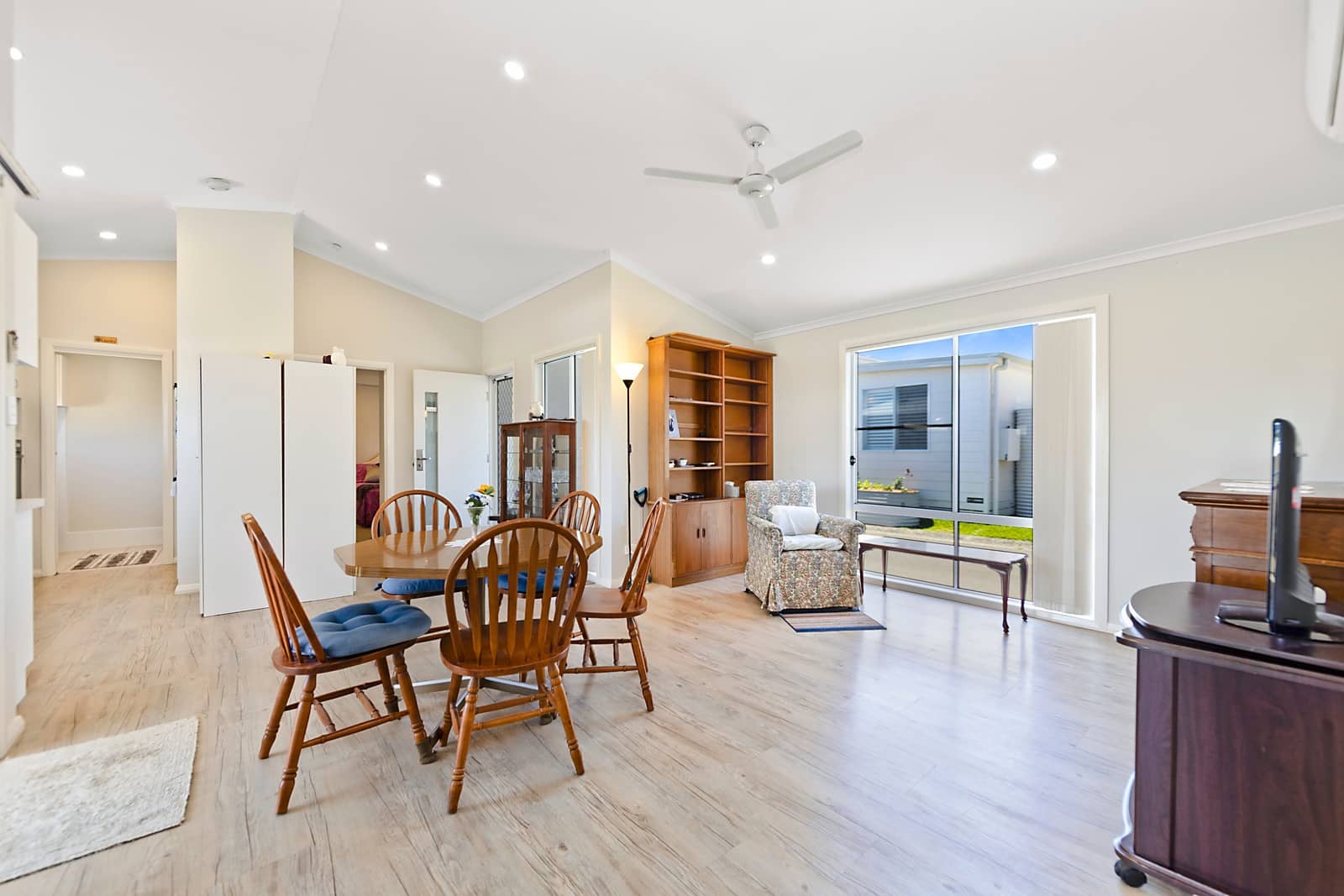 An open-plan living and dining area in an Ingenia Lifestyle home, with light wood-look flooring and a window showing another home.