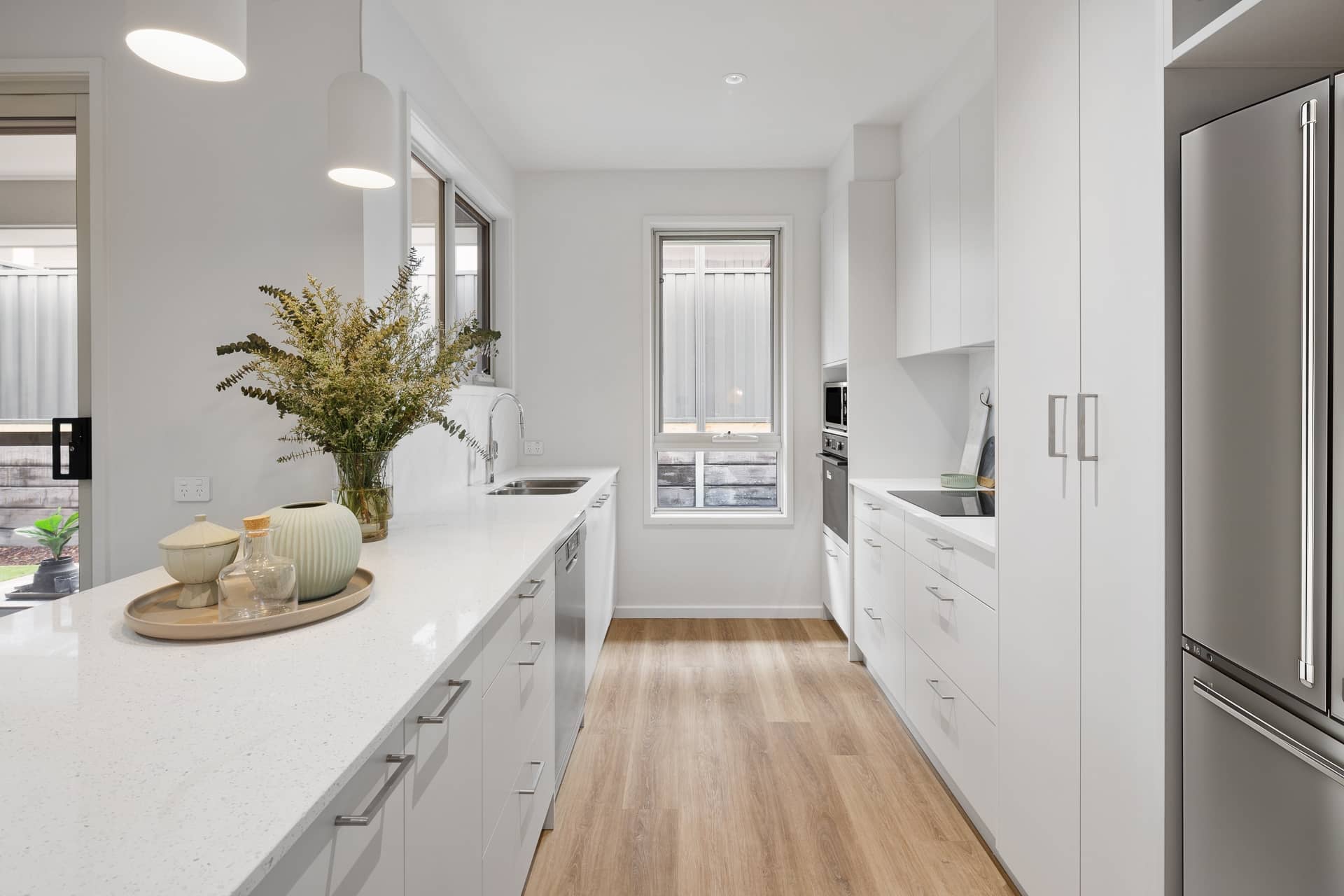Modern kitchen in an Ingenia Lifestyle home with white cabinetry, light benchtops, wood-look floor, and stainless steel appliances.