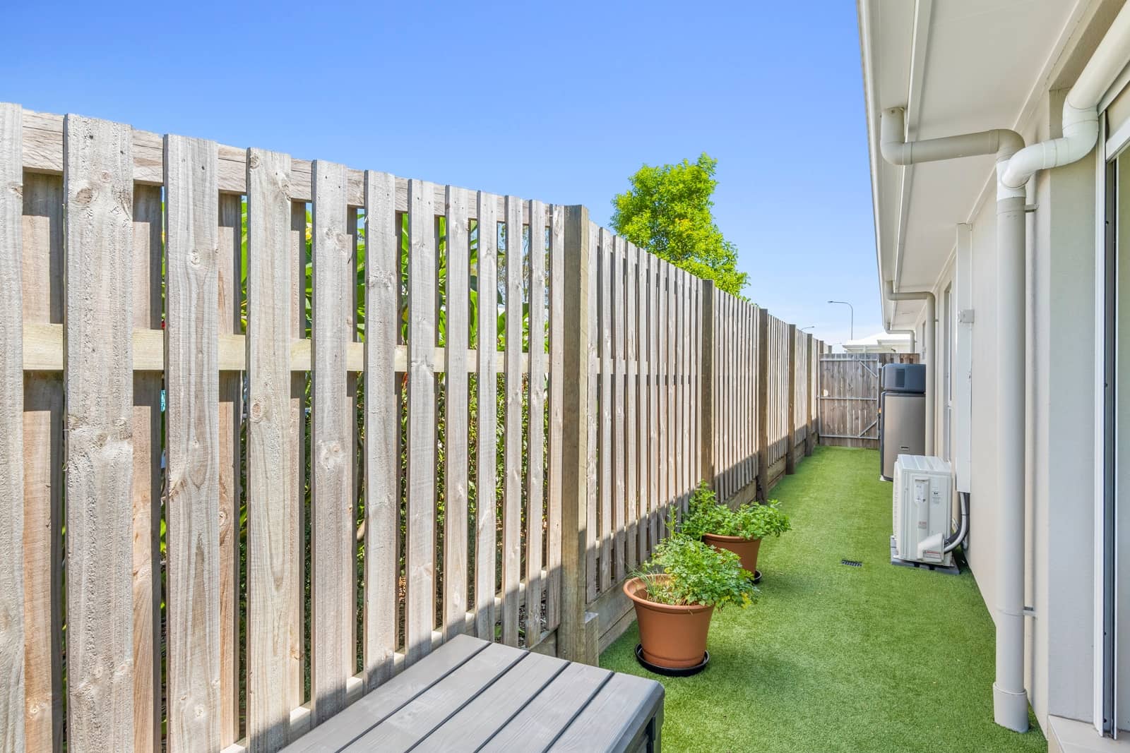 A low-maintenance backyard with artificial turf, a wooden fence, and two potted plants.