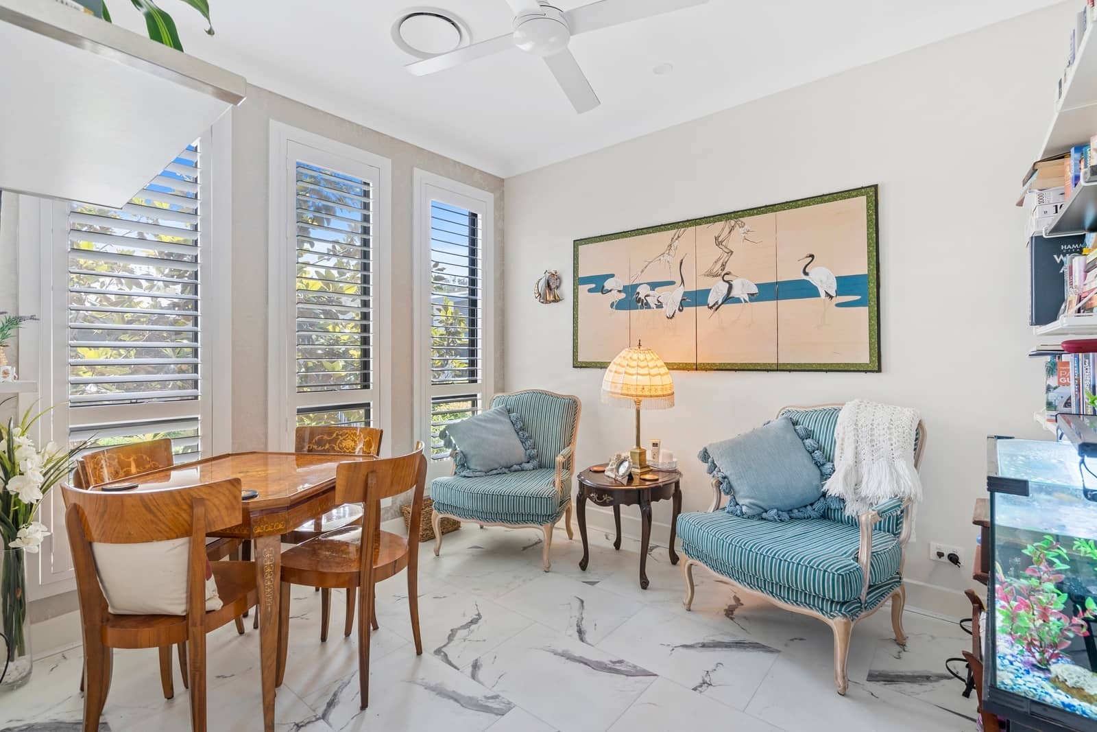 A wooden dining table and chairs sit in front of shuttered windows in this Ingenia Lifestyle home.