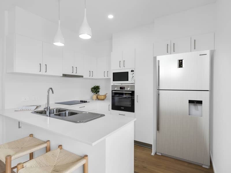 A clean, modern kitchen in an Ingenia Lifestyle community, featuring white cabinets, stainless steel appliances, and a double sink.