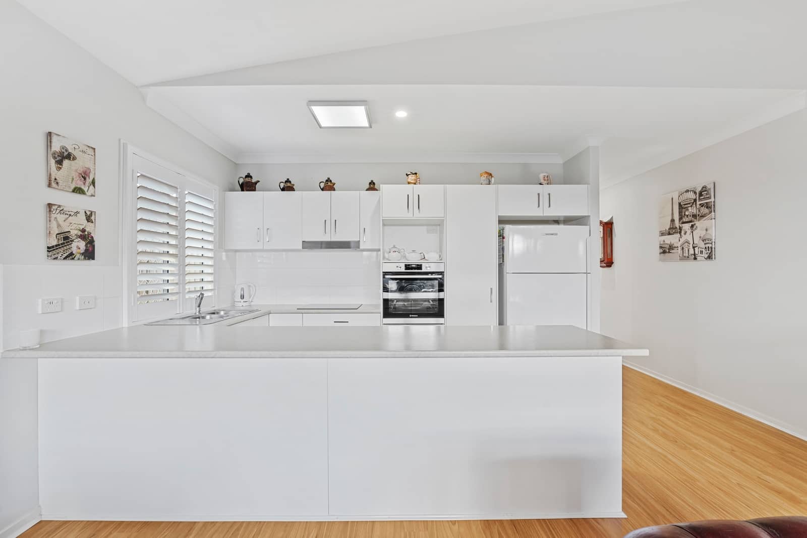 Modern white kitchen with island, appliances, and wood flooring in an Ingenia Lifestyle community.