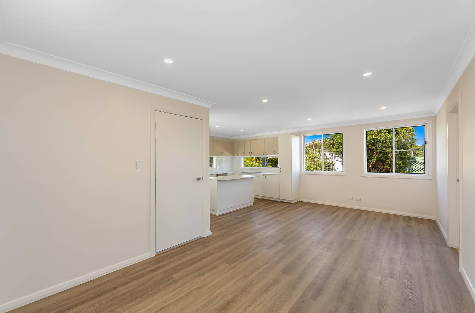 Bright, open-plan living area and modern kitchen in an Ingenia Lifestyle home, featuring wood-look flooring and windows with green views.