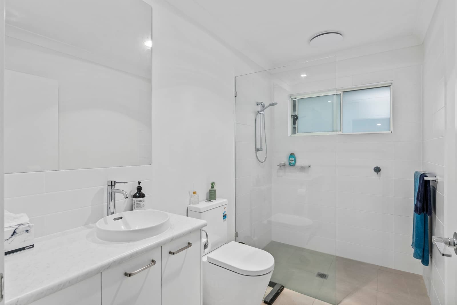 Modern white bathroom in an Ingenia Lifestyle home with a vanity, toilet, and walk-in shower with a glass screen and window.