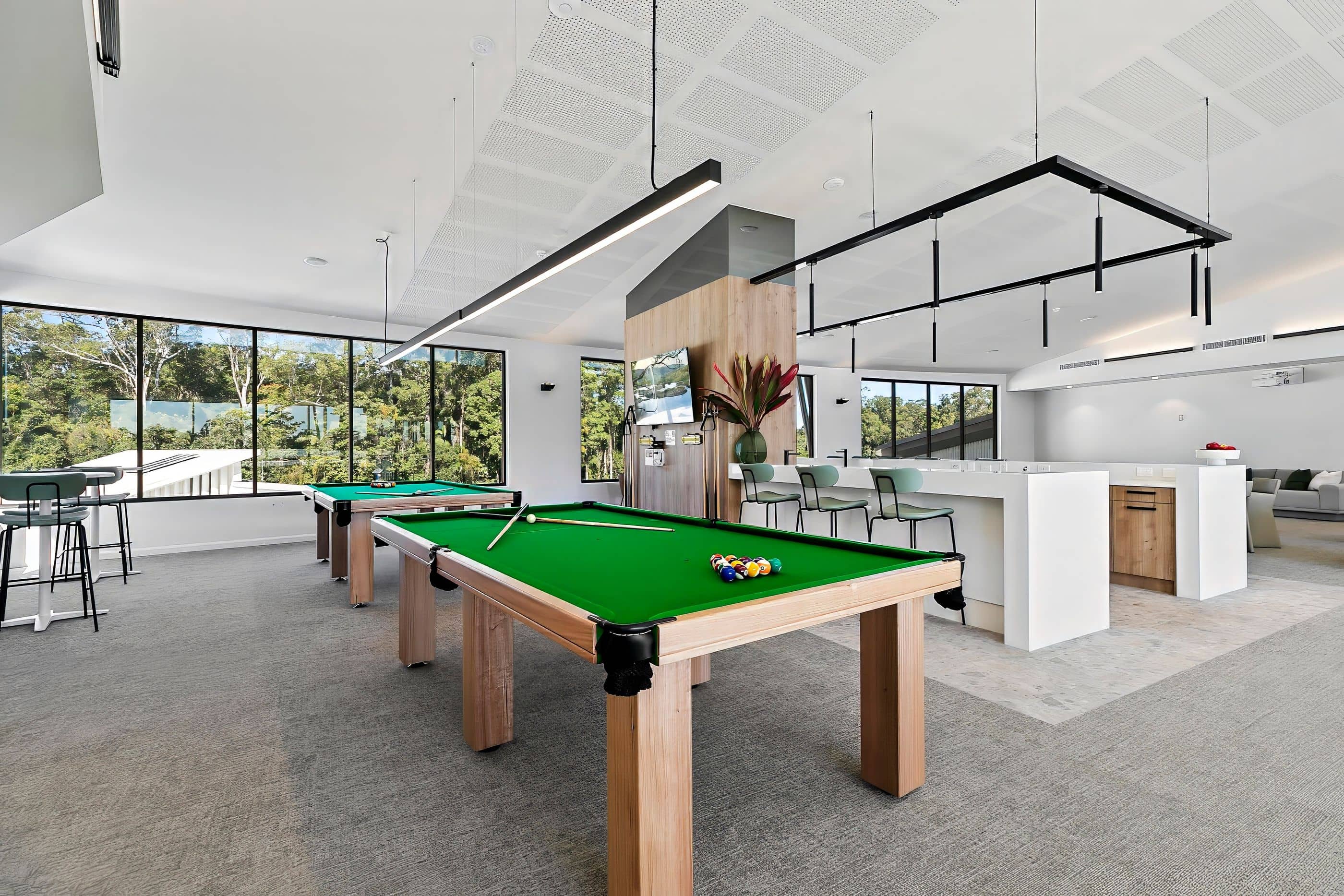 An Ingenia Lifestyle community hub with two billiard tables, a modern kitchen/bar, and seating overlooking natural bushland.
