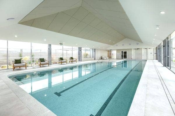 Indoor swimming pool in an Ingenia Lifestyle community with clear blue water, lane lines, lounge chairs, and large windows.