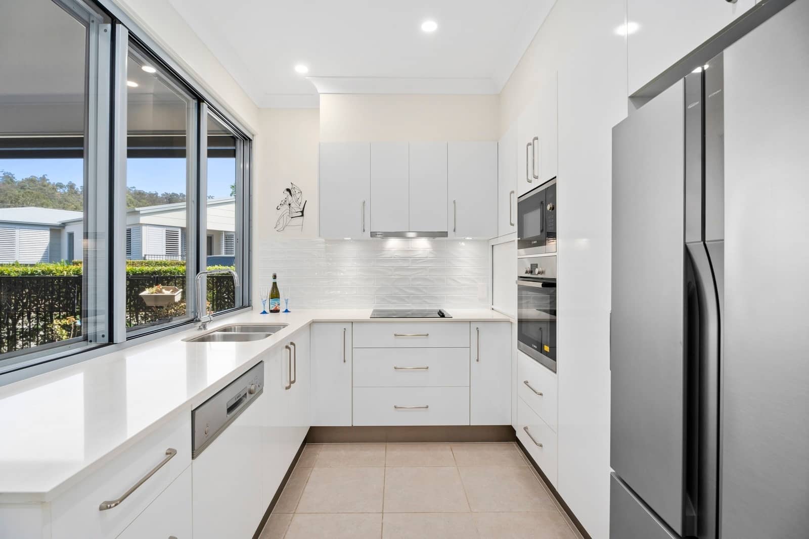 Modern kitchen in an Ingenia Lifestyle home with white cabinets, stainless steel appliances, and a large window overlooking the community.