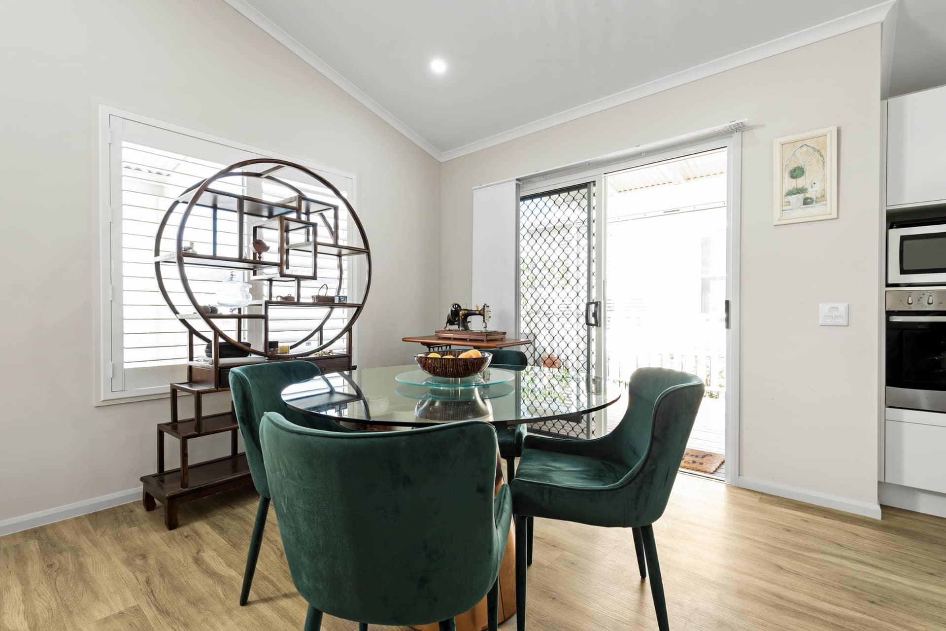 Dining space in an Ingenia Lifestyle home featuring a glass table, green velvet chairs, decorative shelf, and outdoor access.