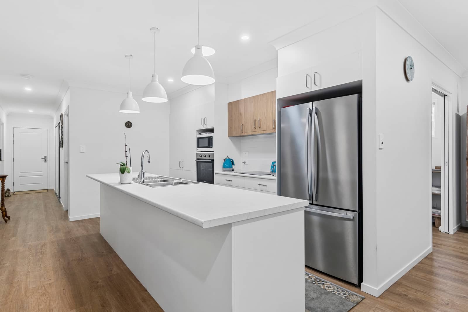 Modern kitchen in an Ingenia Lifestyle home with white cabinetry, large island, stainless steel appliances, and wood-look flooring.