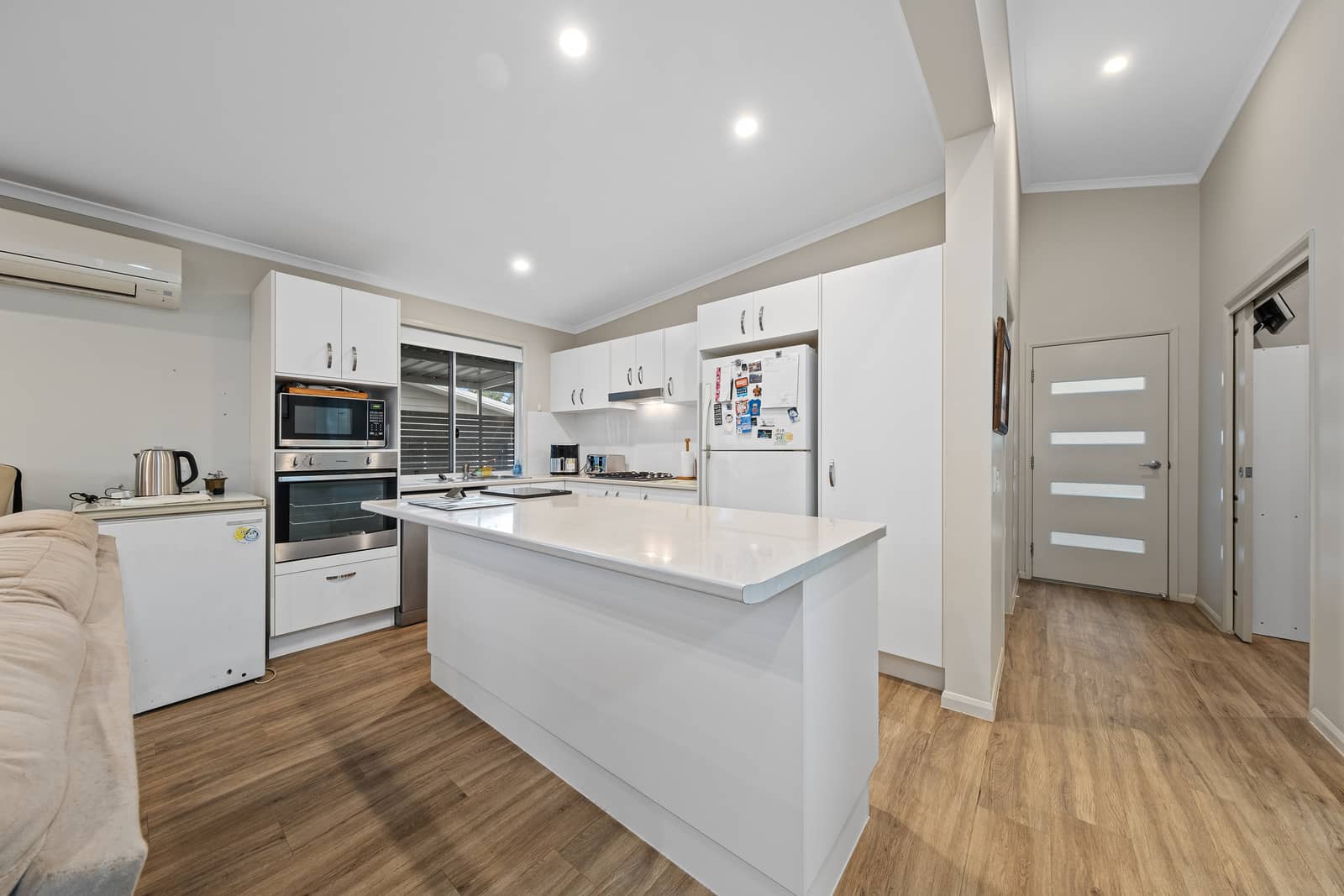 Modern kitchen in an Ingenia Lifestyle home with white cabinets, large island, built-in appliances, and timber-look flooring.