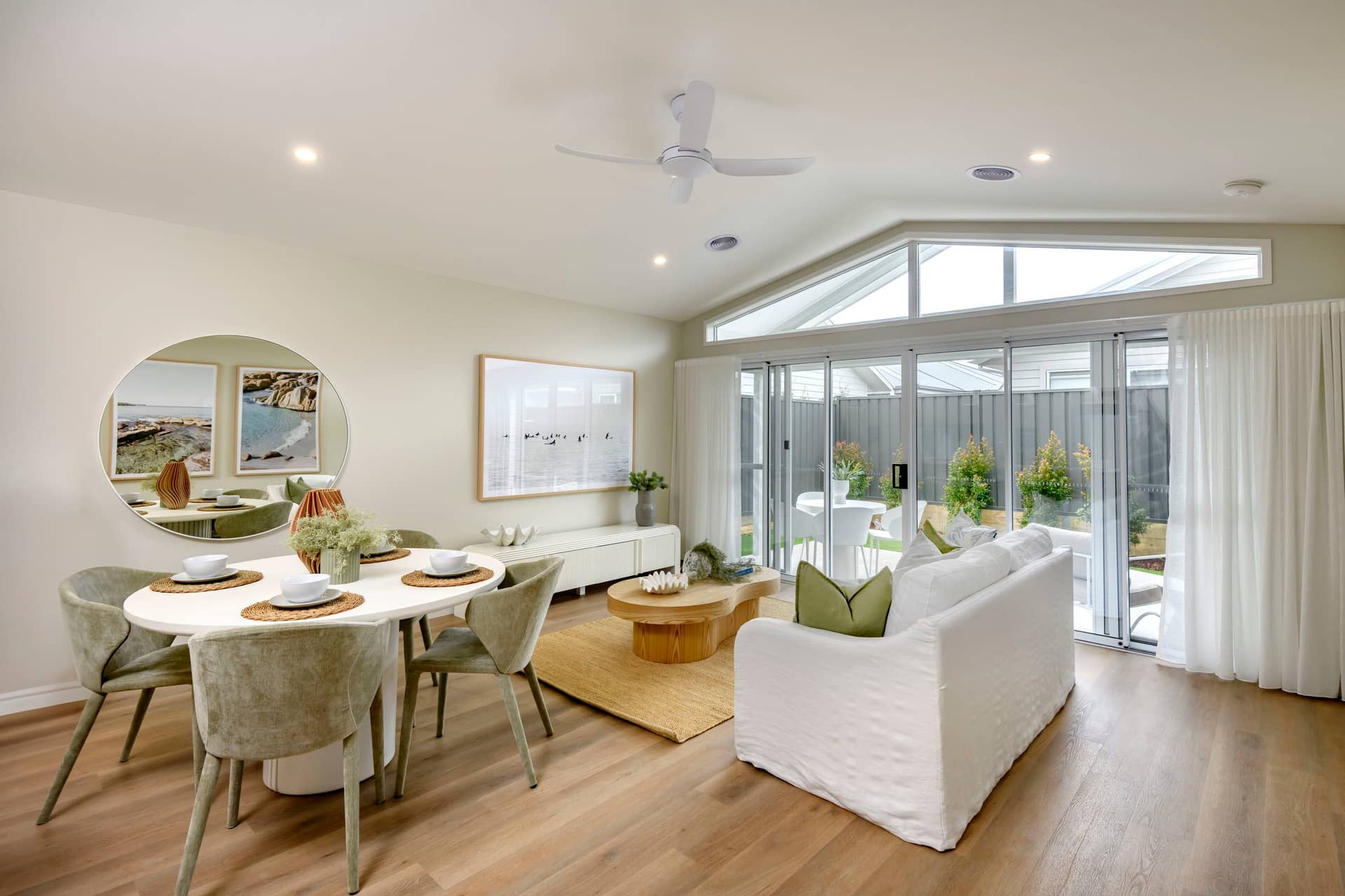A bright, modern living and dining area with a white sectional sofa and a round dining table.