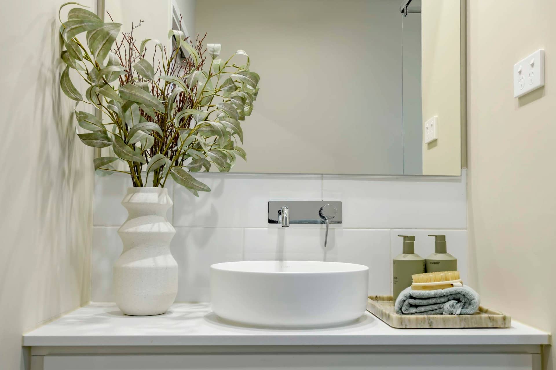 A modern bathroom vanity with a white vessel sink, chrome tap, and decorative plant.