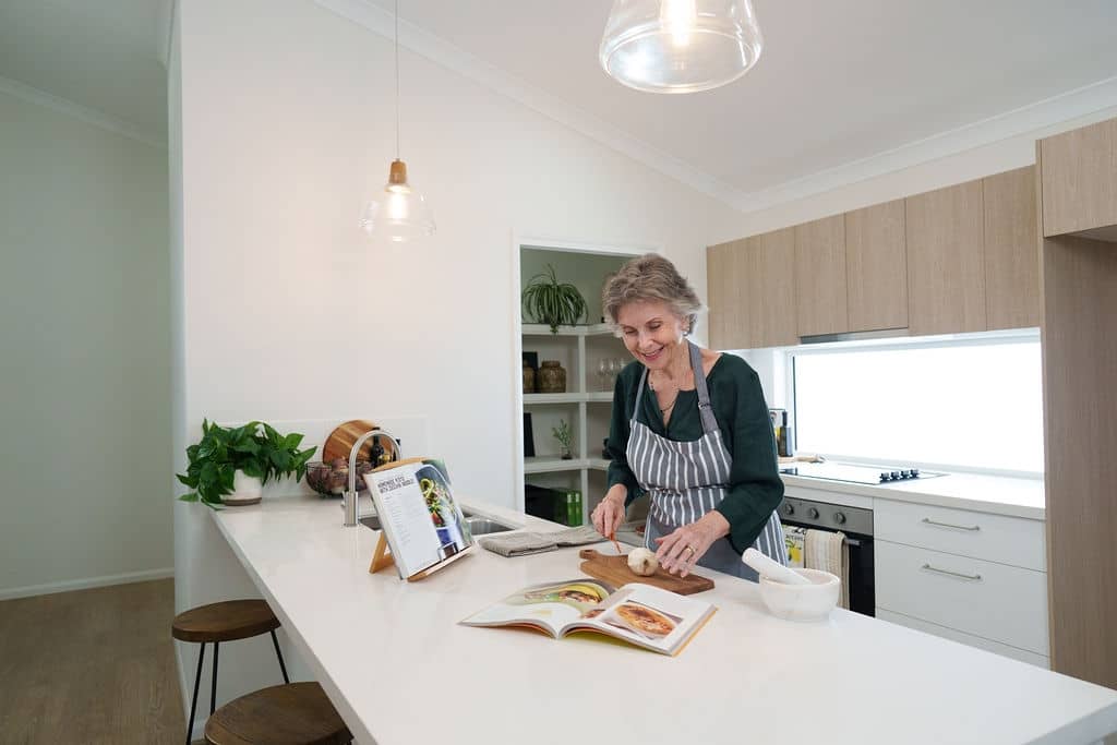 A resident chopping ingredients in a bright, modern kitchen of an Ingenia Lifestyle home, with an island bench.