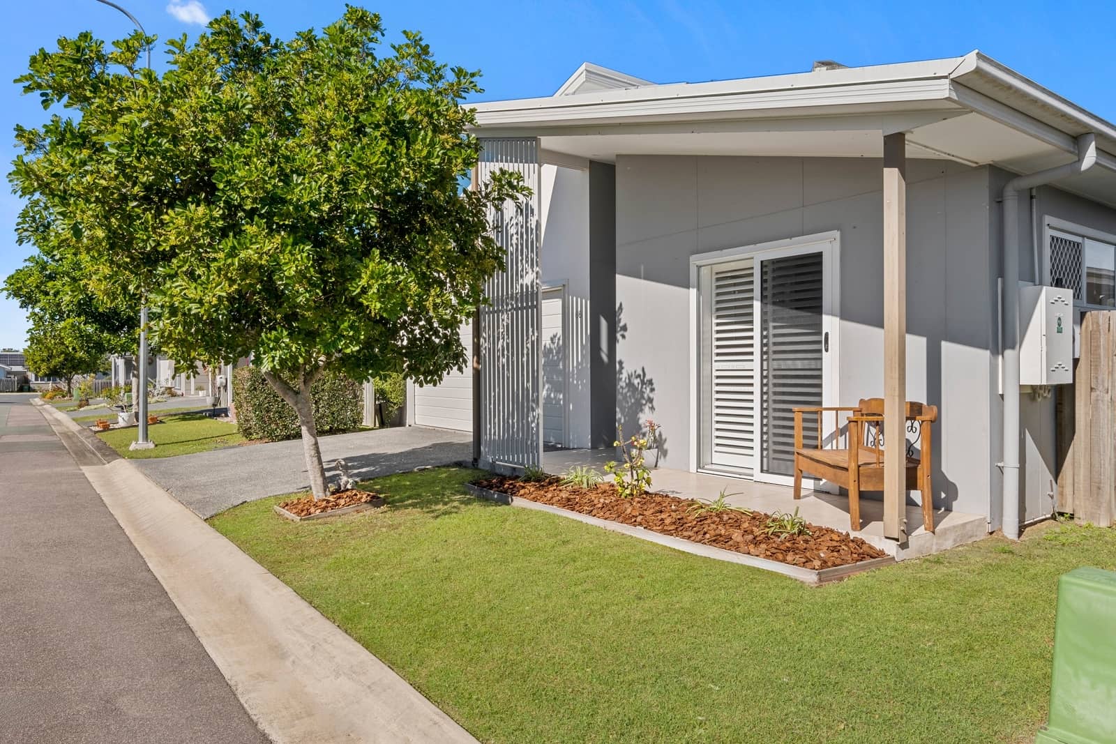 A modern land lease home entrance with a sliding door, wooden bench and neat garden beds.
