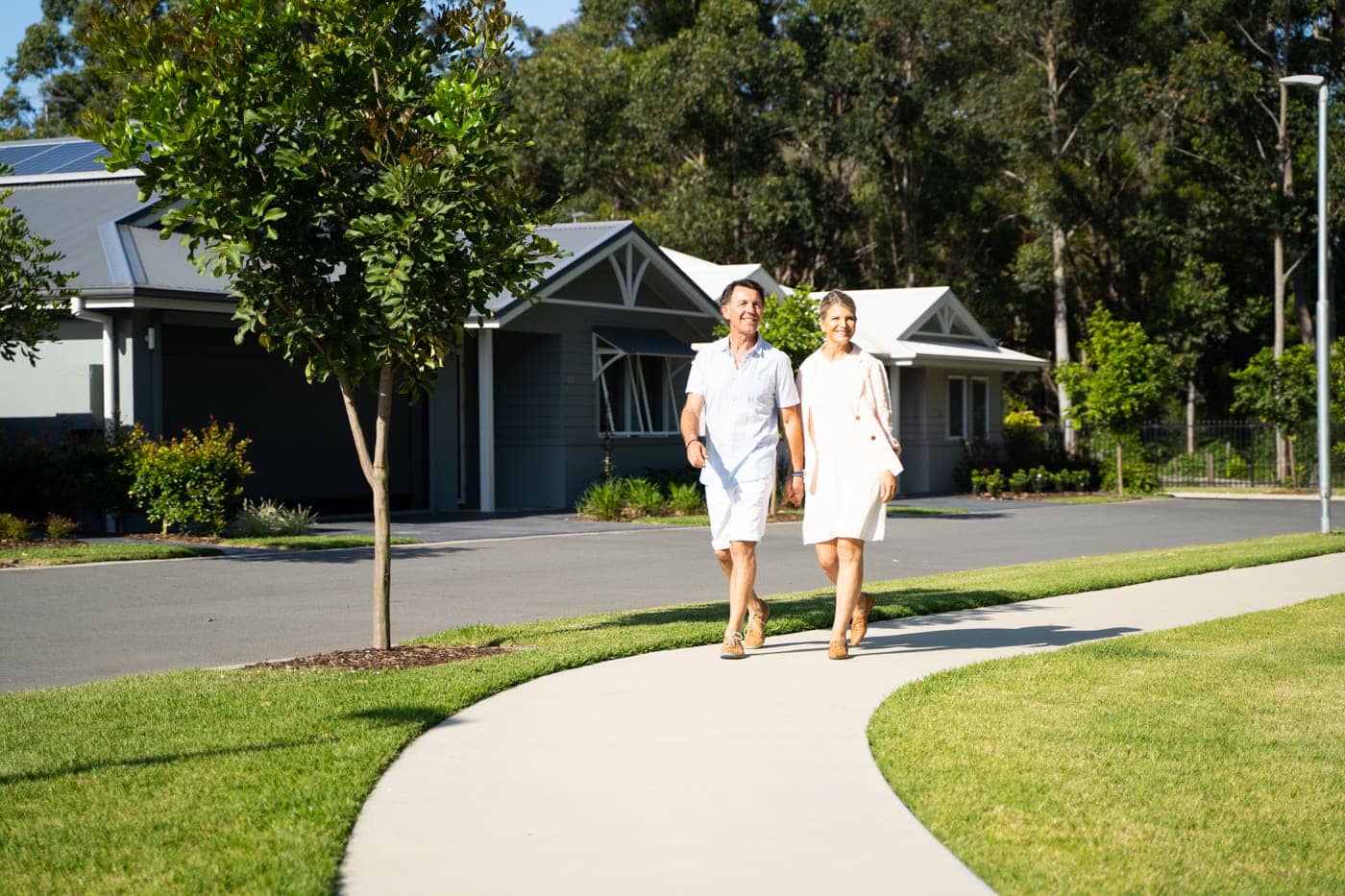A couple walks on a pathway in an Ingenia Lifestyle community with homes in the background.