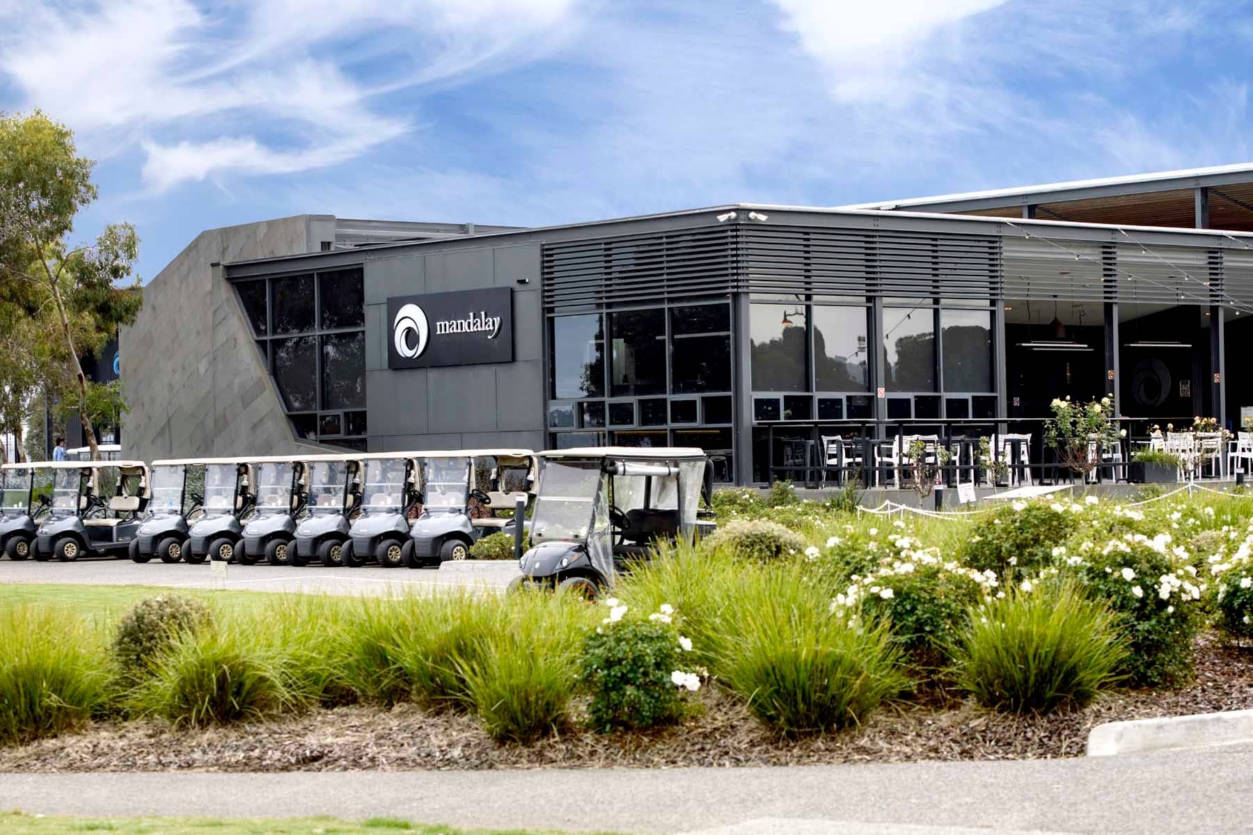A row of golf carts parked in front of the Mandalay building with outdoor seating and landscaped gardens.