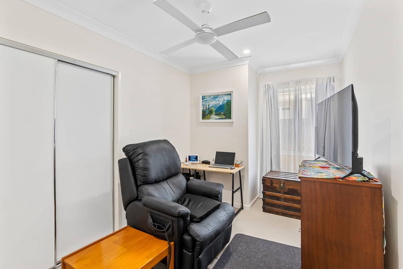 A black leather recliner chair is next to a desk with a laptop and a framed landscape painting on the wall in an Ingenia Lifestyle home.