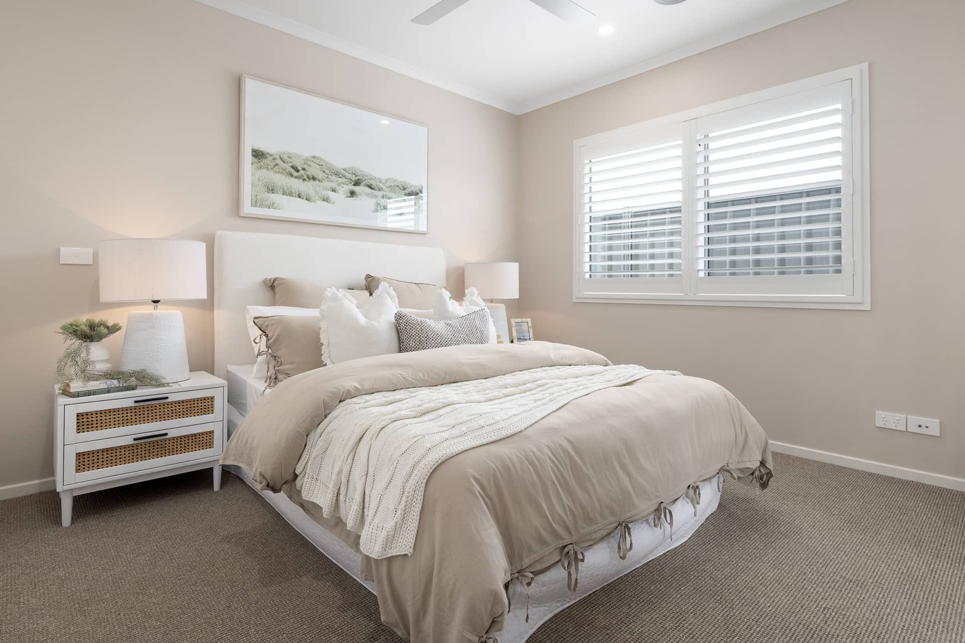 Bedroom with a bed, bedside table, window with shutters, and wall art in an Ingenia Lifestyle community.