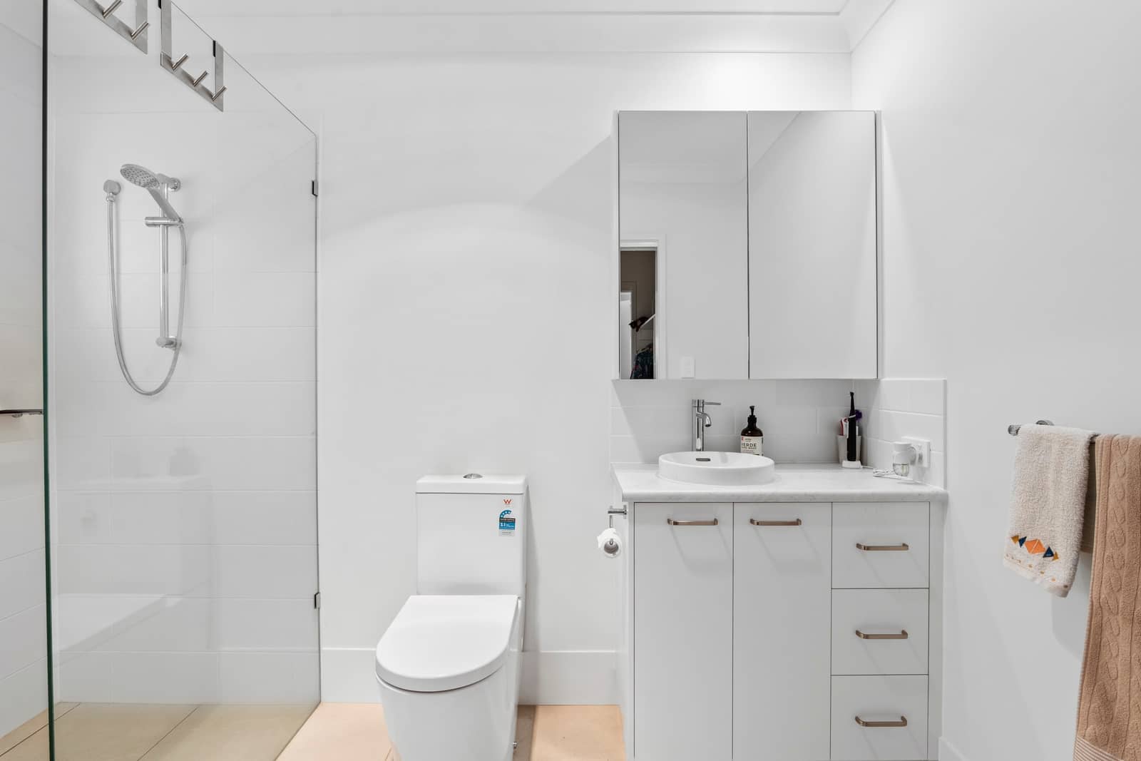 A modern white bathroom in an Ingenia Lifestyle home, featuring a glass shower, toilet, and vanity with storage and a mirrored cabinet.