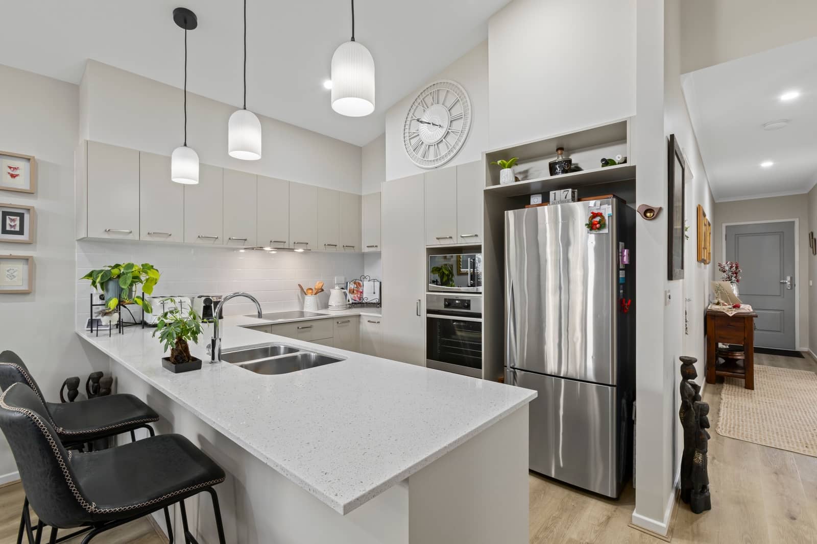 Modern kitchen with light grey cabinets, stainless steel appliances, and a breakfast bar with black stools.