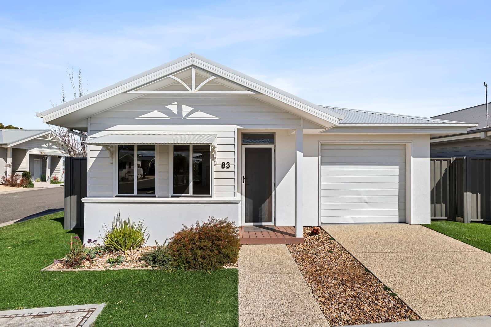 A white, low-maintenance land lease home in an Ingenia Lifestyle community with a garage, path, and landscaped garden.