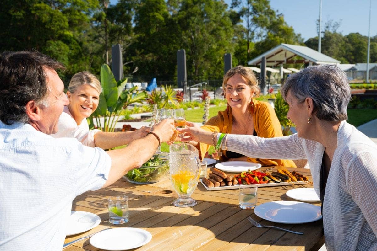 Four people raising glasses for a toast at a table with food outdoors in an Ingenia Lifestyle community.