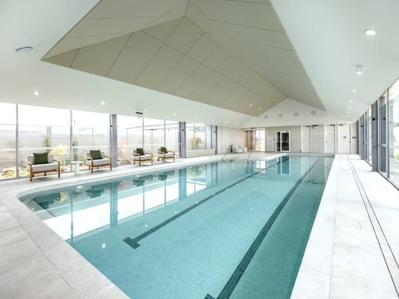 Indoor swimming pool with lane markers and lounge chairs in an Ingenia Lifestyle community shared facility.